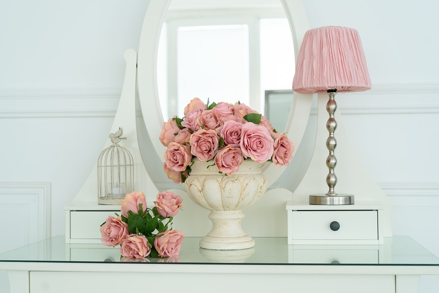 Bouquet of pink roses in vase and pink lamp on white boudoir table 