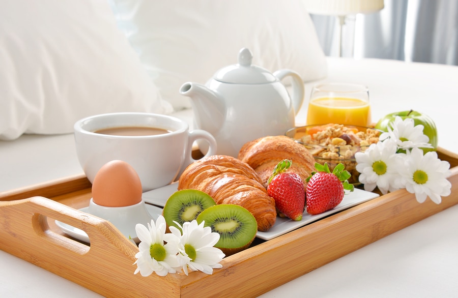 Breakfast tray in bed on luxury hotel bed sheets with pillows