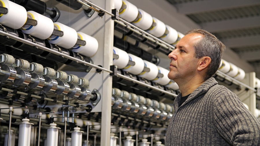 Portrait of an engineer in front of automated machines for thread manufacturing.