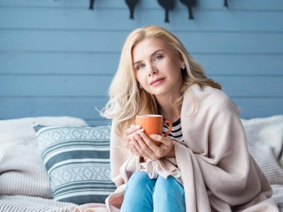 Beautiful blond woman sitting in bedroom covered with warm blanket