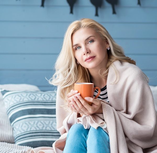 Beautiful blond woman sitting in bedroom covered with warm blanket