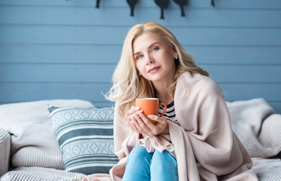 Beautiful blond woman sitting in bedroom covered with warm blanket