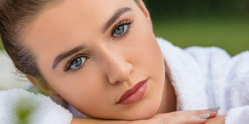 Beautiful young woman relaxing in robe outside at health spa