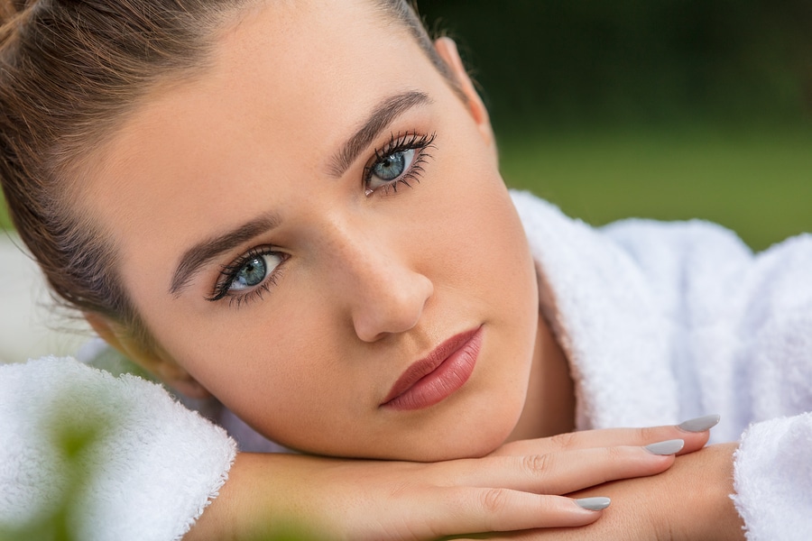 Beautiful young woman relaxing in robe outside at health spa