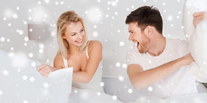 beautiful couple having pillow fight in snow white bedroom with white Christmas snow flakes special effect