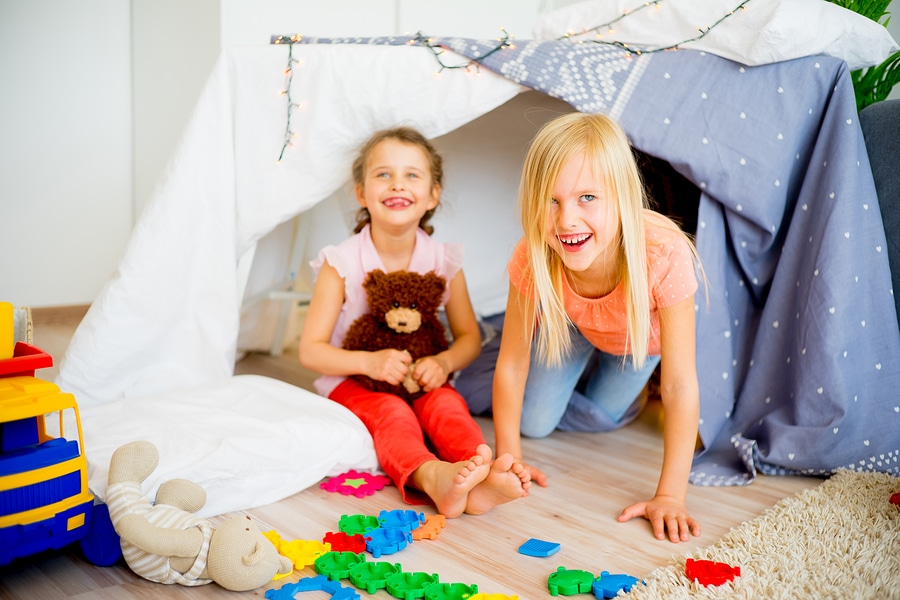 Girls playing in pillow fort made of blankets sheets and pillows