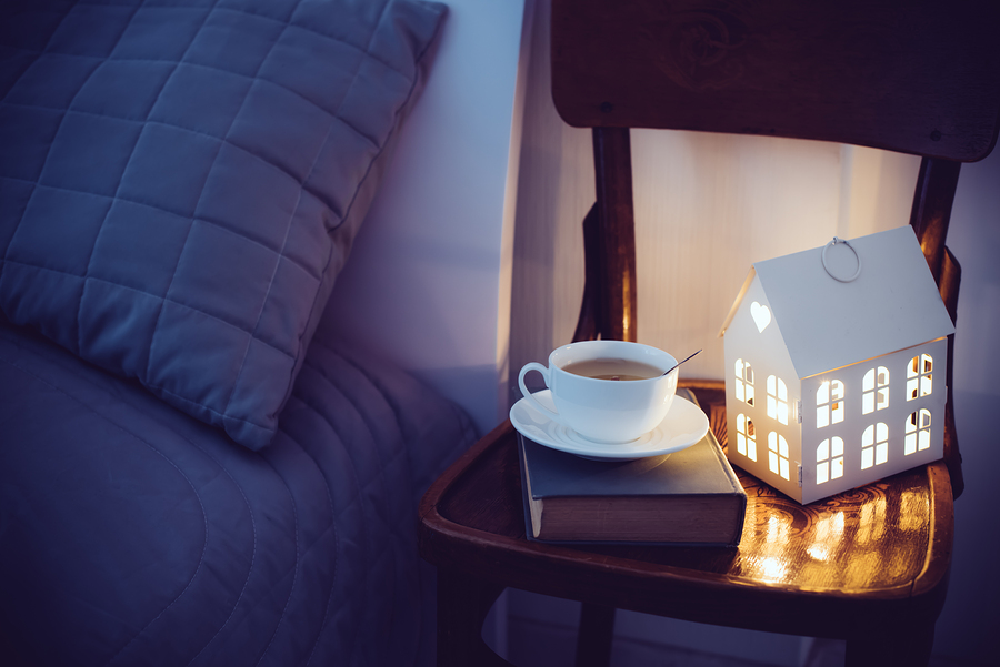 Cozy evening bedroom interior, cup of tea and a night light on the bedside table. Home