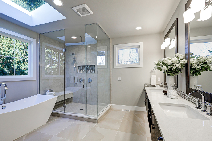 Spacious bathroom in gray tones with heated floors freestanding tub walk-in shower double sink vanity double mirrors and skylight