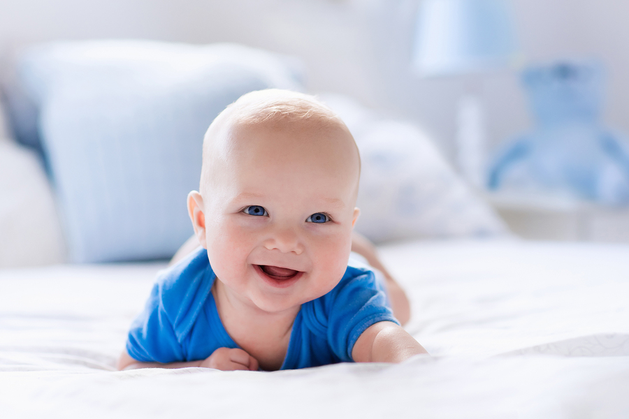 Adorable baby boy in white sunny bedroom showing textile and bedding for kids