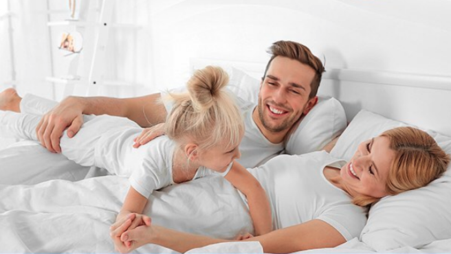 parents and little girl on parents bed on sobel westex white bed sheets and pillows