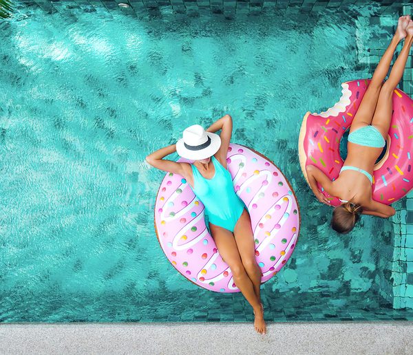 Swimming pool from overhead with mom and daughter lounging on doughnut shaped floats.