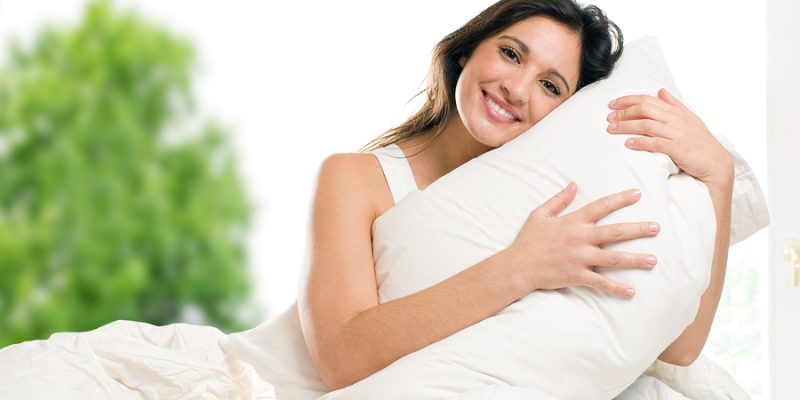happy woman embracing her fluffy bed pillow in bed in the morning