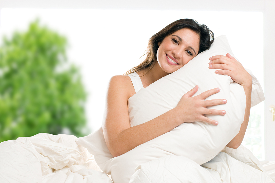 happy woman embracing her fluffy bed pillow in bed in the morning