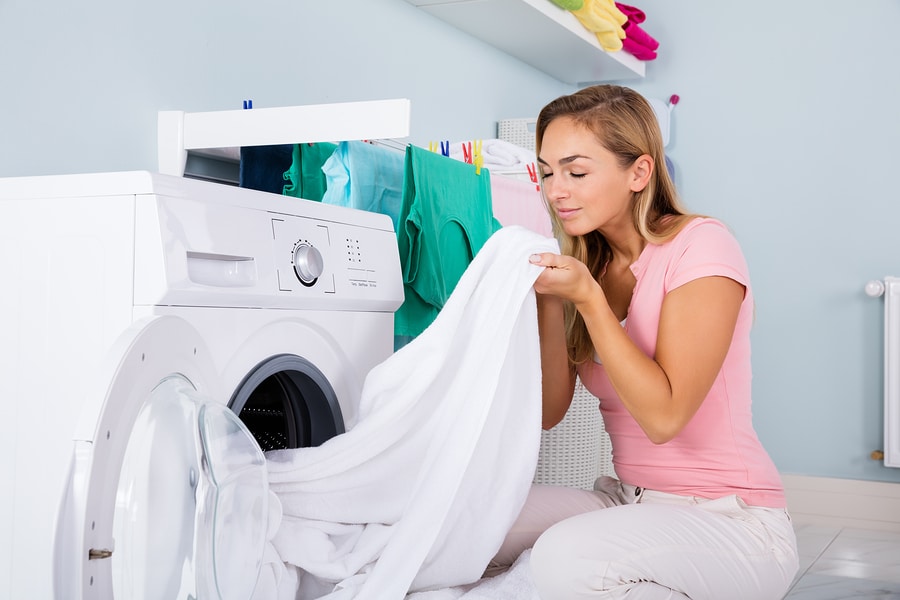 Young Woman Smelling Freshly laundered white bed sheet as she removes it from the dryer