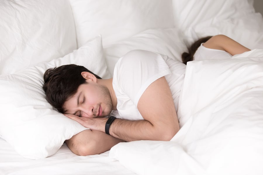 young couple asleep in luxury bed with white bed sheet set and six fluffy white luxury pillows