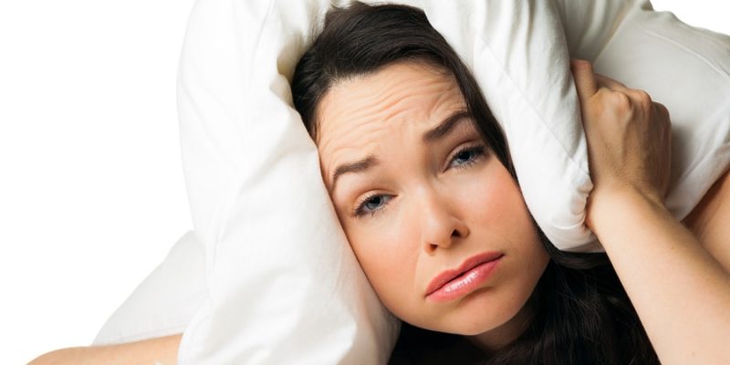 woman with hotel pillow over her head can't sleep due to noise