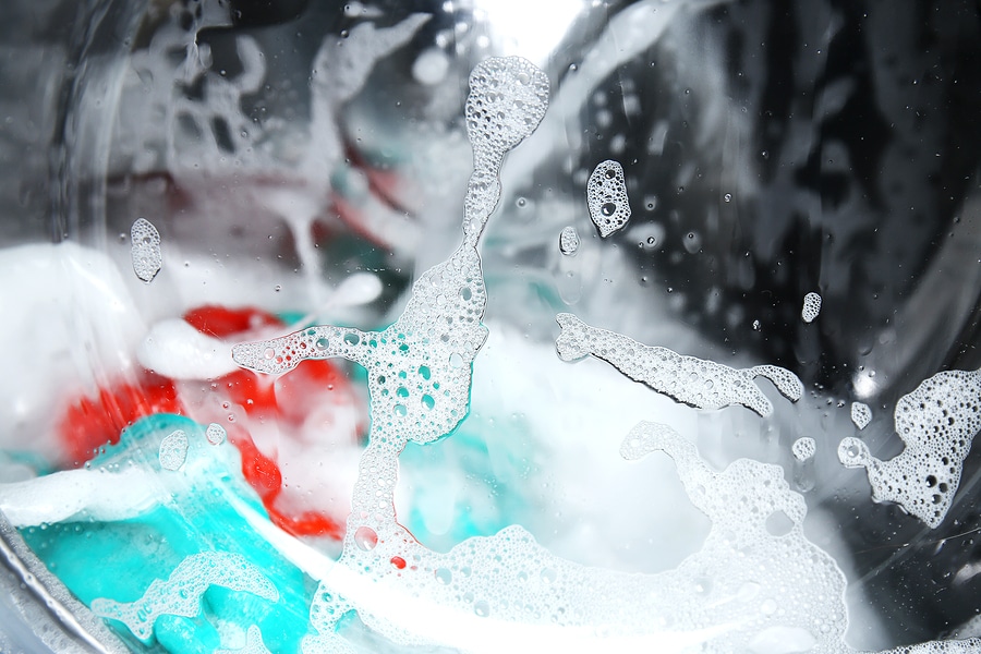 Soapy window view of bed sheets and other clothes in a washing machine