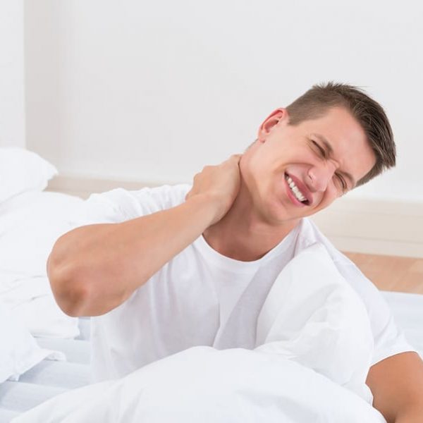 Young Man Suffering From stiff neck In Bedroom