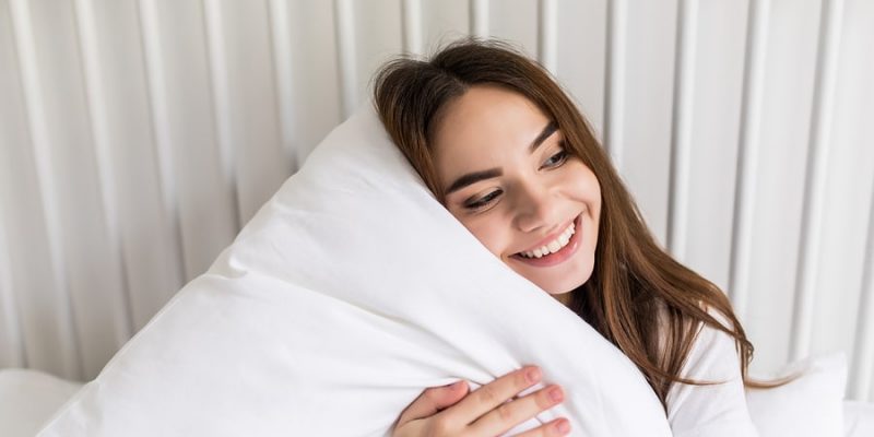 Young woman hugging a fluffy white pillow in a pillow protector