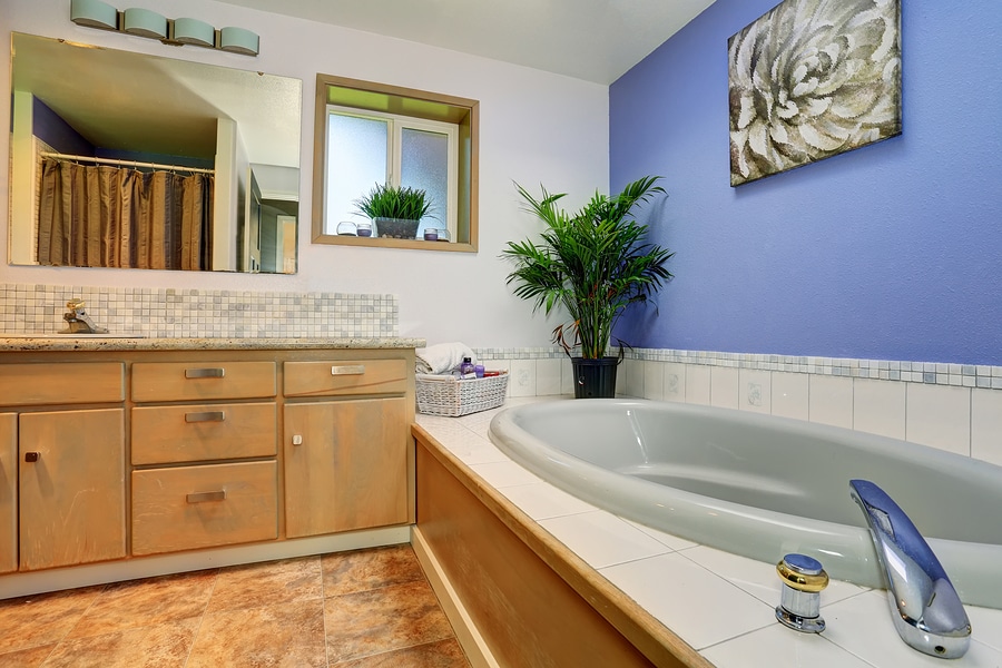 Simple and summery blue bathroom interior with tile trim bath tub and decorative plant pots