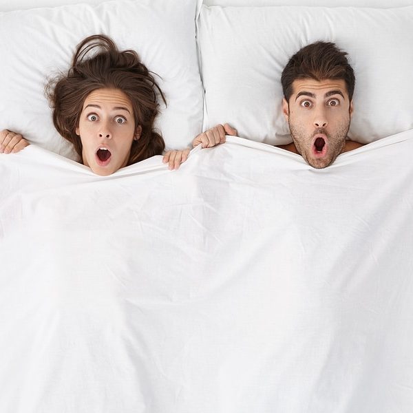 man and woman looking surprised in bed on white pillows