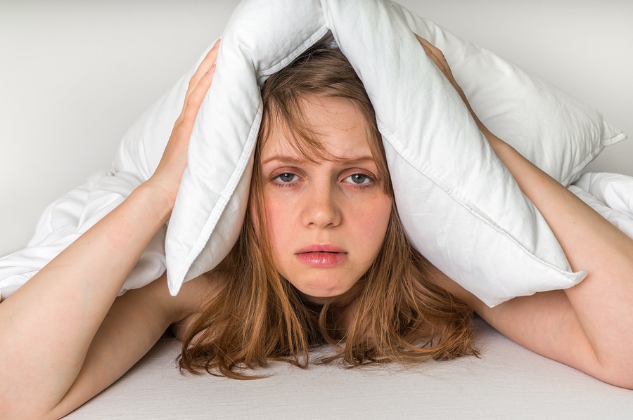 Young woman in bed covering ears with saggy old pillow