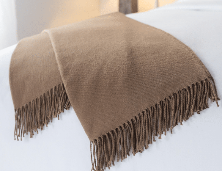 Brown Sobel alpaca blanket with fringe folded on hotel bed