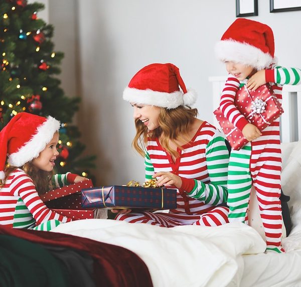 Children and mom in pajamas giving mom a wrapped gift in her bed on Christmas morning