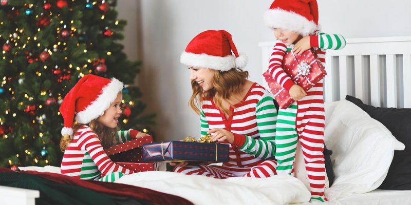 Children and mom in pajamas giving mom a wrapped gift in her bed on Christmas morning