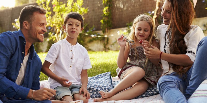 smiling famiy of 4 picnicking on old bedsheet or blanket in backyard