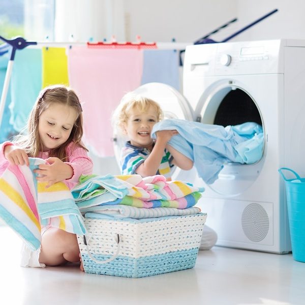 Children in laundry room sorting clean towels in front of dryer.