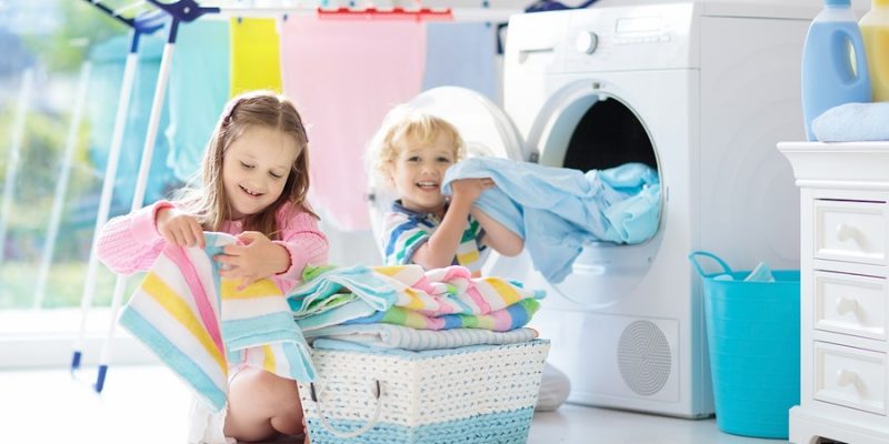 Children in laundry room sorting clean towels in front of dryer.