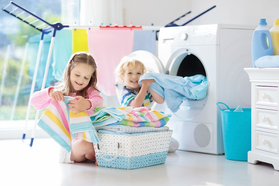 Children in laundry room sorting clean towels in front of dryer.