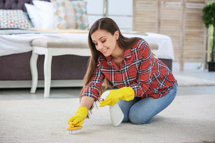 Young woman cleaning carpet with brush in bedroom