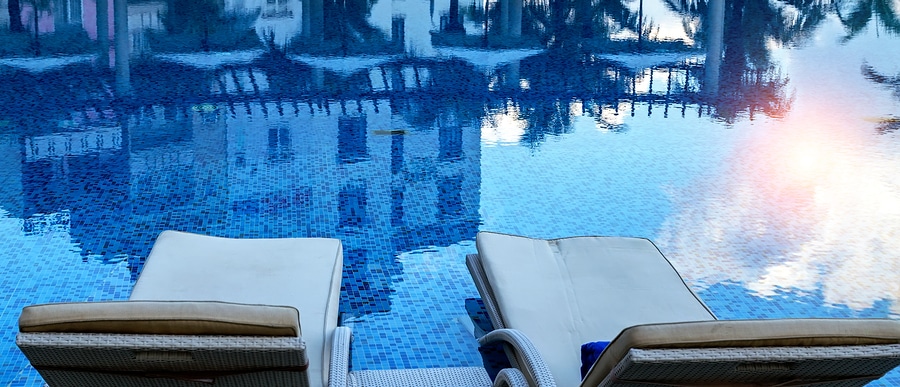 refelctive pool at sunset with two chaise longue chairs over the water