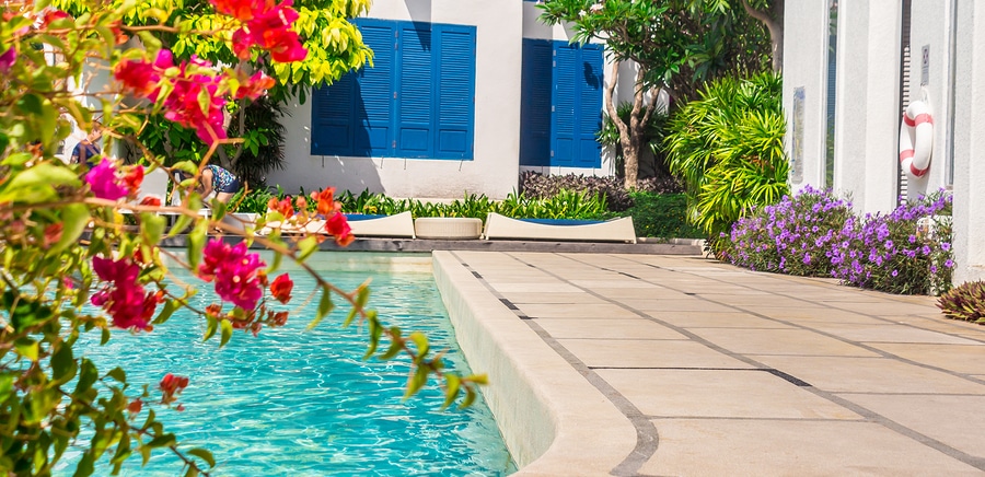 Beautiful flowers around pool patio white stucco home with blue shutters peaceful summer afternoon