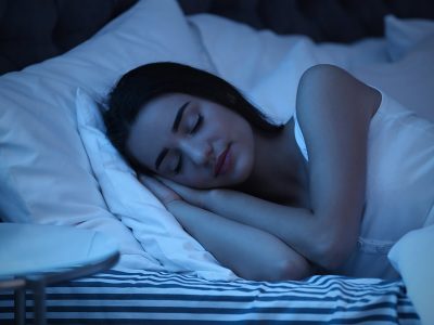 Relaxed smiling young woman sleeping in bed on two soft pillows in dark bedroom