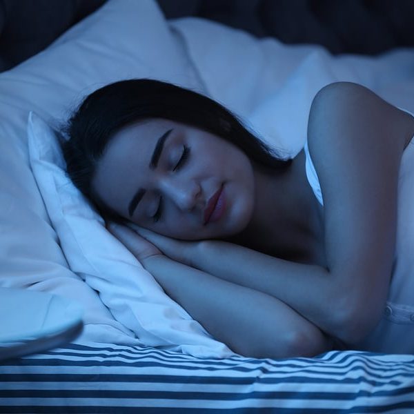 Relaxed smiling young woman sleeping in bed on two soft pillows in dark bedroom