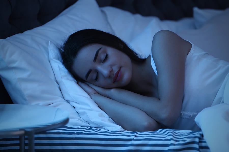 Relaxed smiling young woman sleeping in bed on two soft pillows in dark bedroom