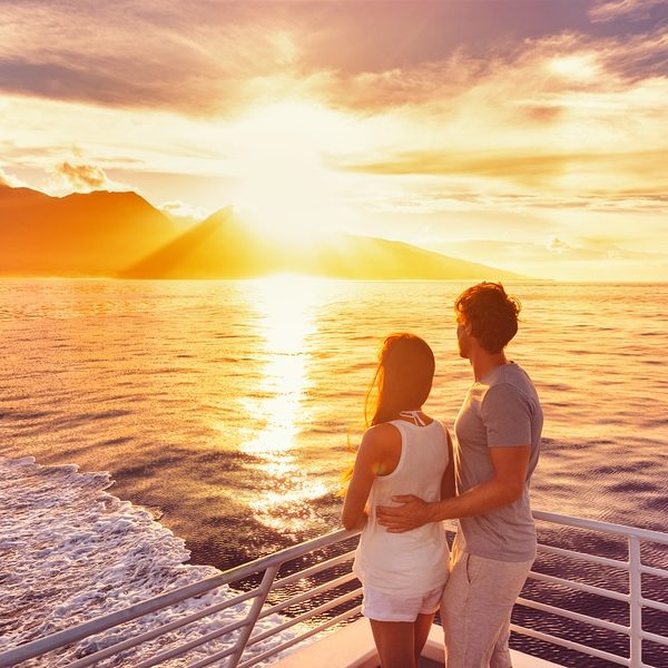 Couple watch sunset from deck of a luxury cruise ship