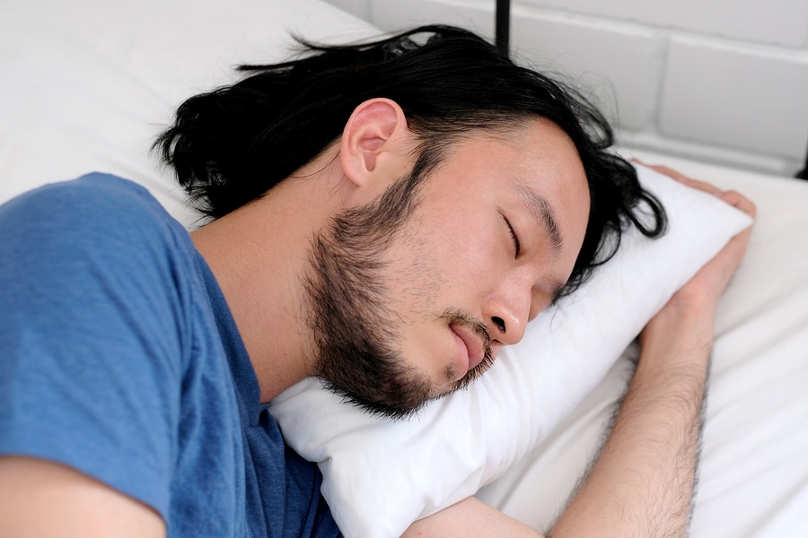  asian man sleeping on standard size pillow in bed in white bedroom