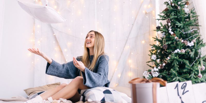 Happy girl in bathrobe tossing her new bellaure duo feather pillow in front of a christmas tree