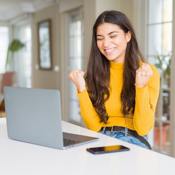 young woman with laptop at kitchen table happy for free shipping online