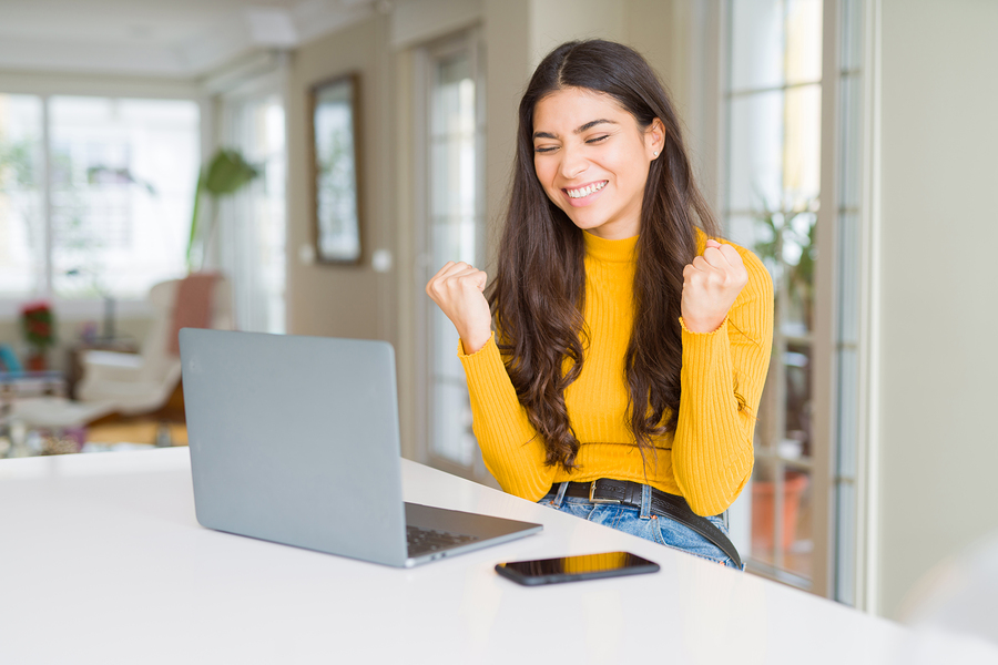 young woman with laptop at kitchen table happy for free shipping online