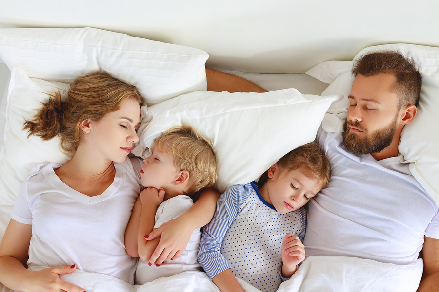 Family of four sleeping sweetly together at home on white Dolce Notte hotel pillows