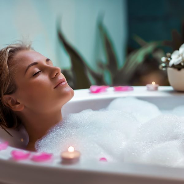 Portrait of a beautiful young woman taking bath with foam and flower petals by candlelight, enjoying dayspa in luxury spa hotel