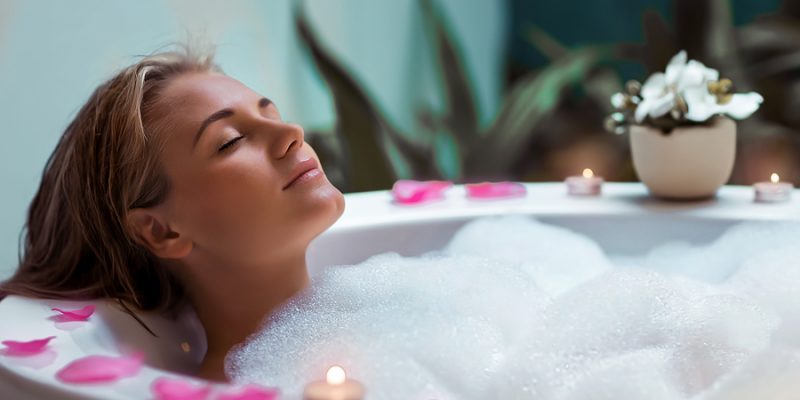 Portrait of a beautiful young woman taking bath with foam and flower petals by candlelight, enjoying dayspa in luxury spa hotel