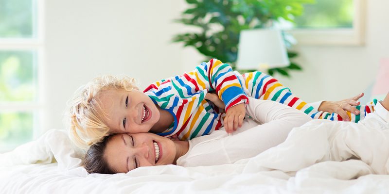 Mother and child playing in bed with clean white egyptian cotton sheets