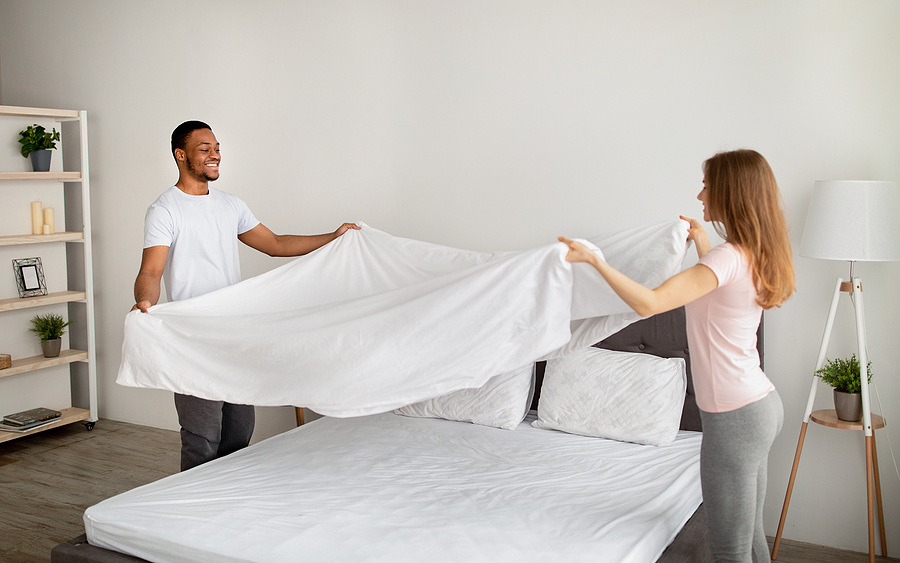 Happy couple sharing the task of putting clean Egyptian cotton sheets on their bed.