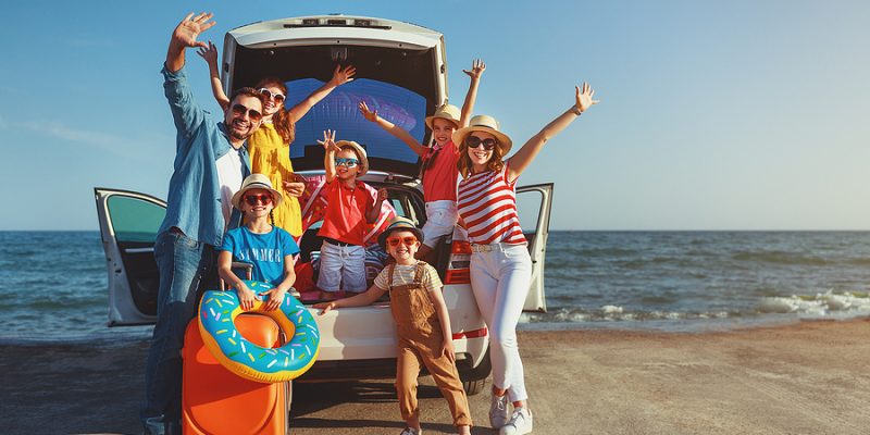 family at the beach waving from the back of their SUV with beach accessories